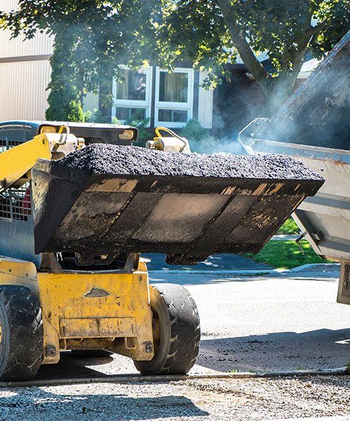 Dump truck and skid steer moving asphalt